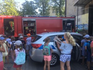Dzieci z zainteresowaniem oglądają radiowóz policyjny oraz wóz strażacki
