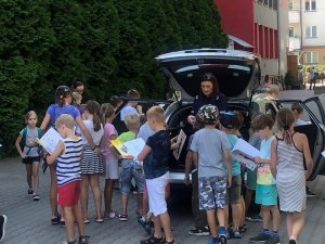 Policjantka przy radiowozie rozdaje dzieciom książeczki edukacyjne Kapitan Wyderka