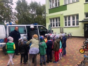 Policjanci pokazują dzieciom policyjny radiowóz oraz policyjne wyposażenie: tarczę, hełm, ochraniacze używane podczas zabezpieczenia imprez masowych.