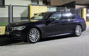 Na zdjęciu samochód marki BMW koloru czarnego zaparkowany przy ogrodzeniu.