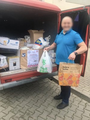 Na zdjęciu policjant Wydziału Kryminalnego Komendy Rejonowej Policji Warszawa VI, który pakuje torby z żywnością do samochodu dostawczego.