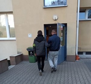 Policjant prowadzi zatrzymanego mężczyznę.