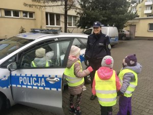 Na zdjęciu dzieci z przedszkola wsiadają do otwartego radiowozu policyjnego, obok dzieci stoi policjantka.