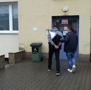 Na zdjęciu policjant prowadzi do budynku komendy zatrzymanego mężczyznę.