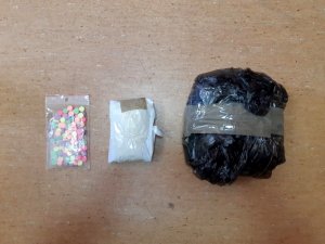 Na zdjęciu zabezpieczone narkotyki, marihuana w pakiecie z czarnej folii, torebka foliowa z białym proszkiem oraz torebka foliowa z kolorowymi tabletkami.