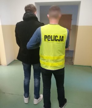 Na zdjęciu na korytarzu żoliborskiego komisariatu policjant prowadzi zatrzymanego mężczyznę.