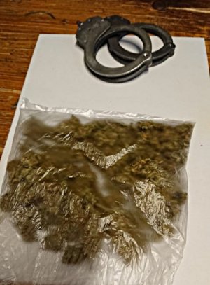 Na blacie stołu leży przeźroczysta torebka foliowa z marihuaną, obok torebki leżą policyjne kajdanki.