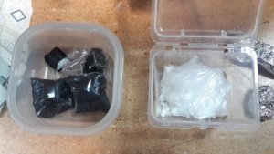 Na zdjęciu dwa pudełka plastikowe z zawartością foliowych woreczków. Woreczki z jednego z pudełek są przeźroczyste dlatego widać w nich zbryloną kokainę.