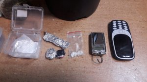 Ułożone w rzędzie telefon komórkowy, waga elektroniczna imitująca telefon komórkowy z klapką, woreczek foliowy z kokainą, dwa zawiniątka z folii aluminiowej i plastikowe pudełko z kokainą.