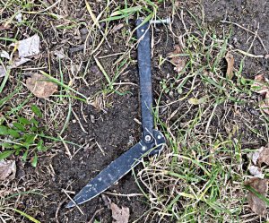 Na trawniku leży nóż metalowy ze składanym ostrzem.