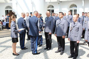 Policjanci stoją w szeregu. Jeden policjant podaje rękę drugiemu.
