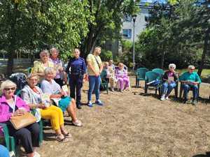 Policjantka stoi przy siedzących seniorach.