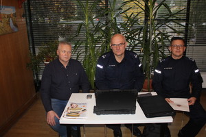 Policjanci i mężczyzna ubrany po cywilnemu siedzą za stołem.