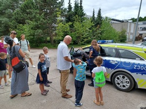 Policyjny radiowóz i ludzie czekający w kolejce.