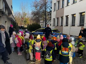 Policjant, opiekunowie i dzieci obok radiowozu.