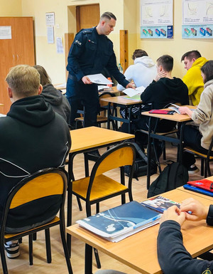 Policjant rozdaje uczniom ulotki.