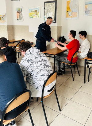 Policjant rozdaje uczniom ulotki.