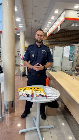 Policjant stoi przy stoliku z ulotkami.