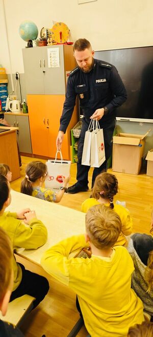 Policjant przekazuje torbę z materiałami edukacyjnymi.