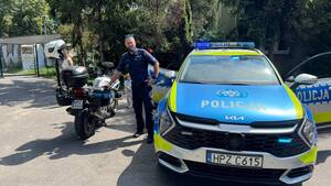Policjant stoi przy motocyklu i radiowozie.