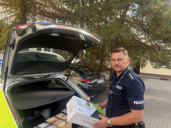 Policjant pakuje książki do radiowozu.